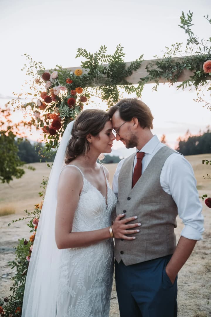Couple in profile about to kiss beneath flowering vines and climbing greenery on an outdoor terrace at dusk