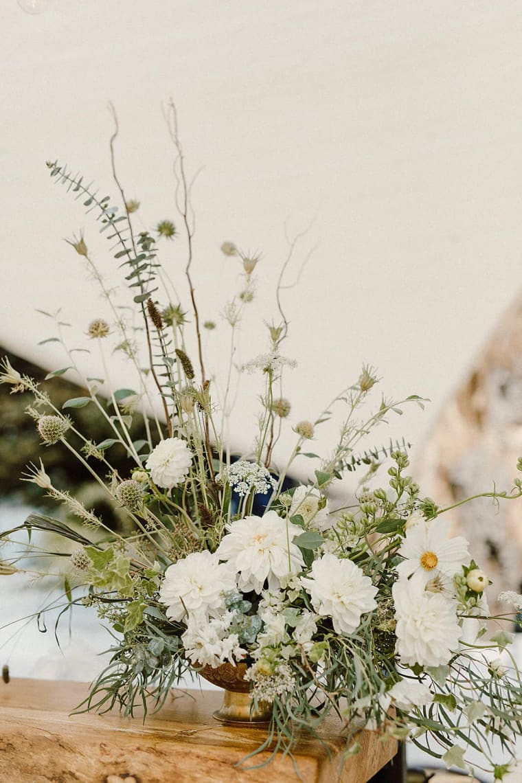 White garden roses and Queen Anne's lace arranged in a brass bowl on a wooden table against cream wall