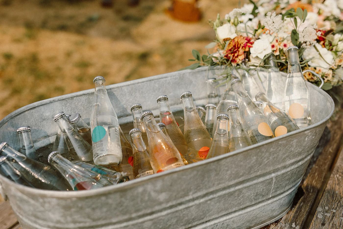 Glass bottles chilling in a metal tub with ice, white flowers and greenery on a wooden table
